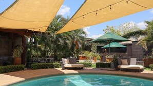 A pool area with lounge chairs and umbrellas, surrounded by palm trees and greenery. - HOTEL LEON INN (León)