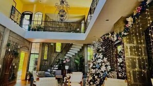 A spacious lobby with a high ceiling, a staircase, and a seating area with wicker chairs. - HOTEL LEON INN (León)