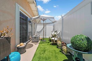 A backyard with artificial grass, a white umbrella, wicker furniture, and a potted plant. - Boho Pink Retreat w/ Kitchen, Patio, Laundry! (San Diego)