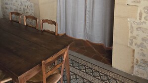 Ein Essbereich mit einem langen Holztisch, vier Holzstühlen, einem grauen Vorhang und einer Steinsäule.