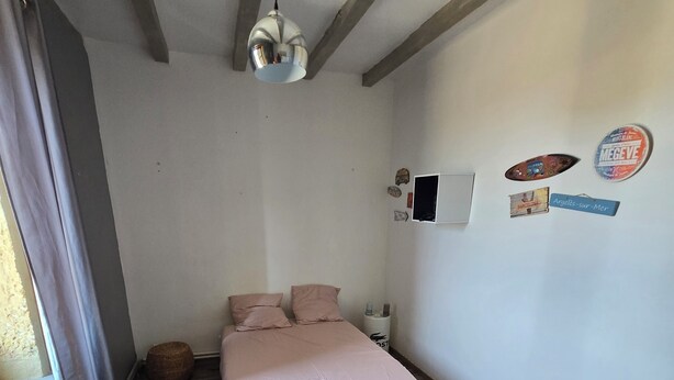 Ein Schlafzimmer mit einem Bett, einem kleinen Nachttisch, einer Lampe, einem an der Wand montierten Fernseher und einem Fenster mit Vorhängen.
