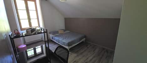 Un apartamento pequeño de una sola habitación, con techo inclinado, cama, escritorio con silla y ventana que proporciona luz natural.