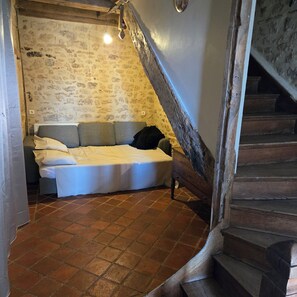 Een slaapkamer met een stenen muur, een bed, een houten trap en een betegelde vloer.