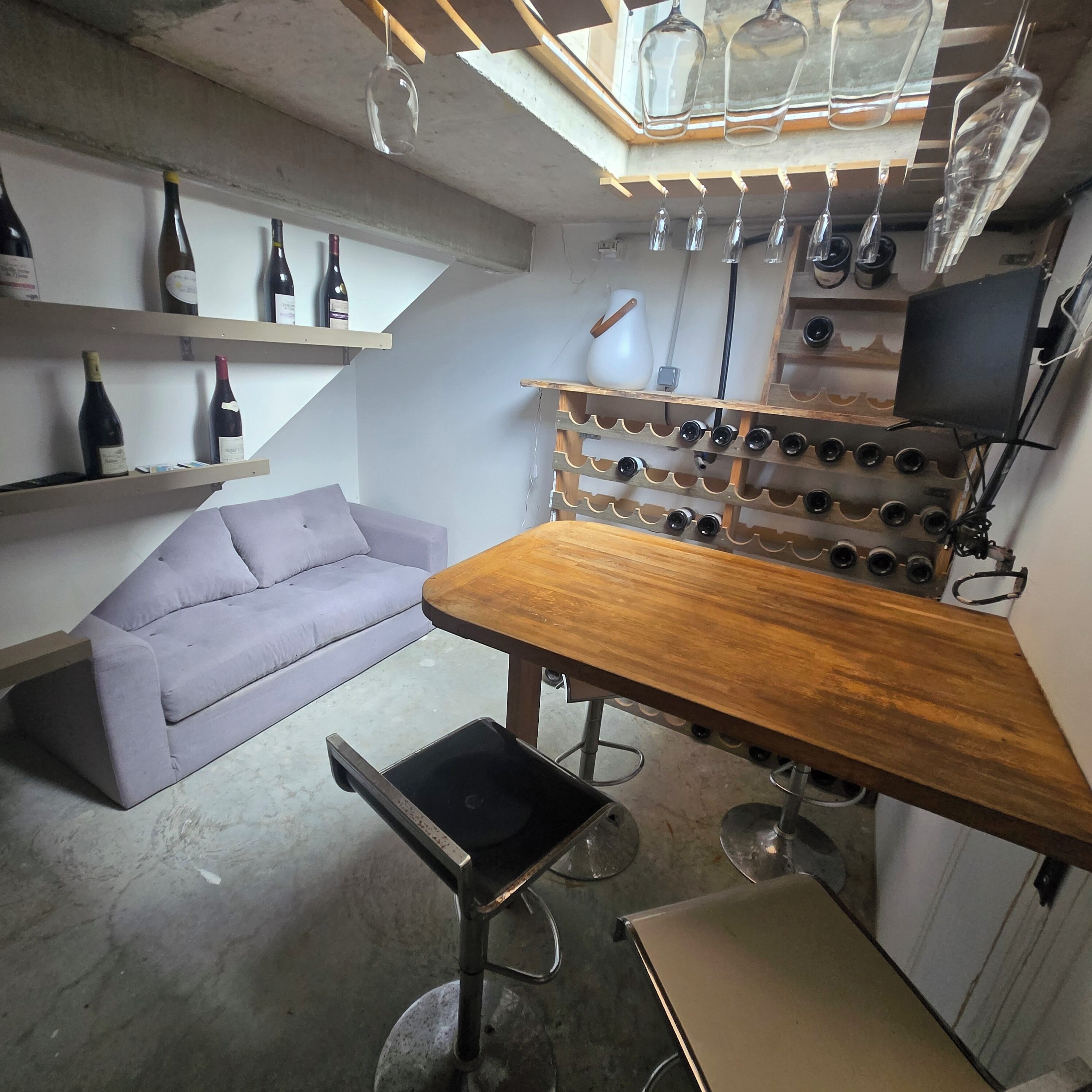 Een kamer met een houten tafel, een bank, een wijnrek en een televisie.