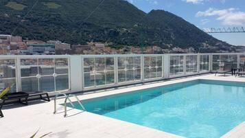 A rooftop pool with a glass enclosure, overlooking a mountainous landscape.