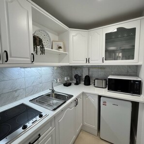 A modern kitchen with white cabinetry, a built-in stove, a microwave, and a dishwasher. - ET - Large Stylish Studio In Centre With Pool (Gibraltar)