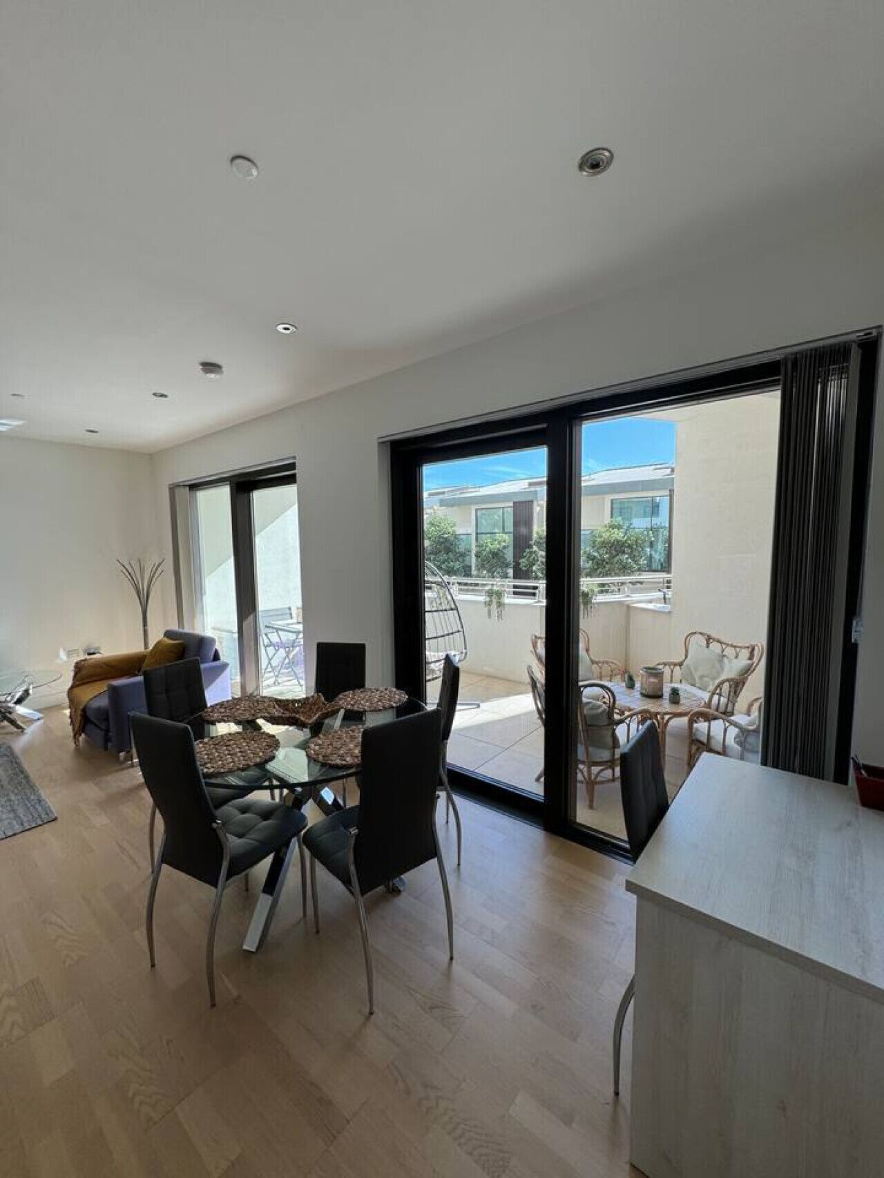 Una sala moderna con comedor, puertas correderas de vidrio que dan a un balcón y vista de un edificio residencial.