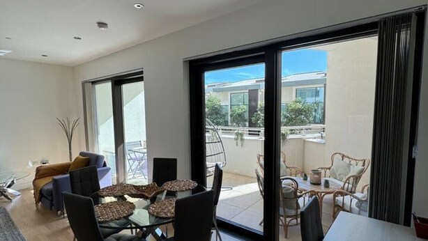 Een moderne woonkamer met een eethoek, grote schuifdeuren naar een balkon en uitzicht op een woongebouw.