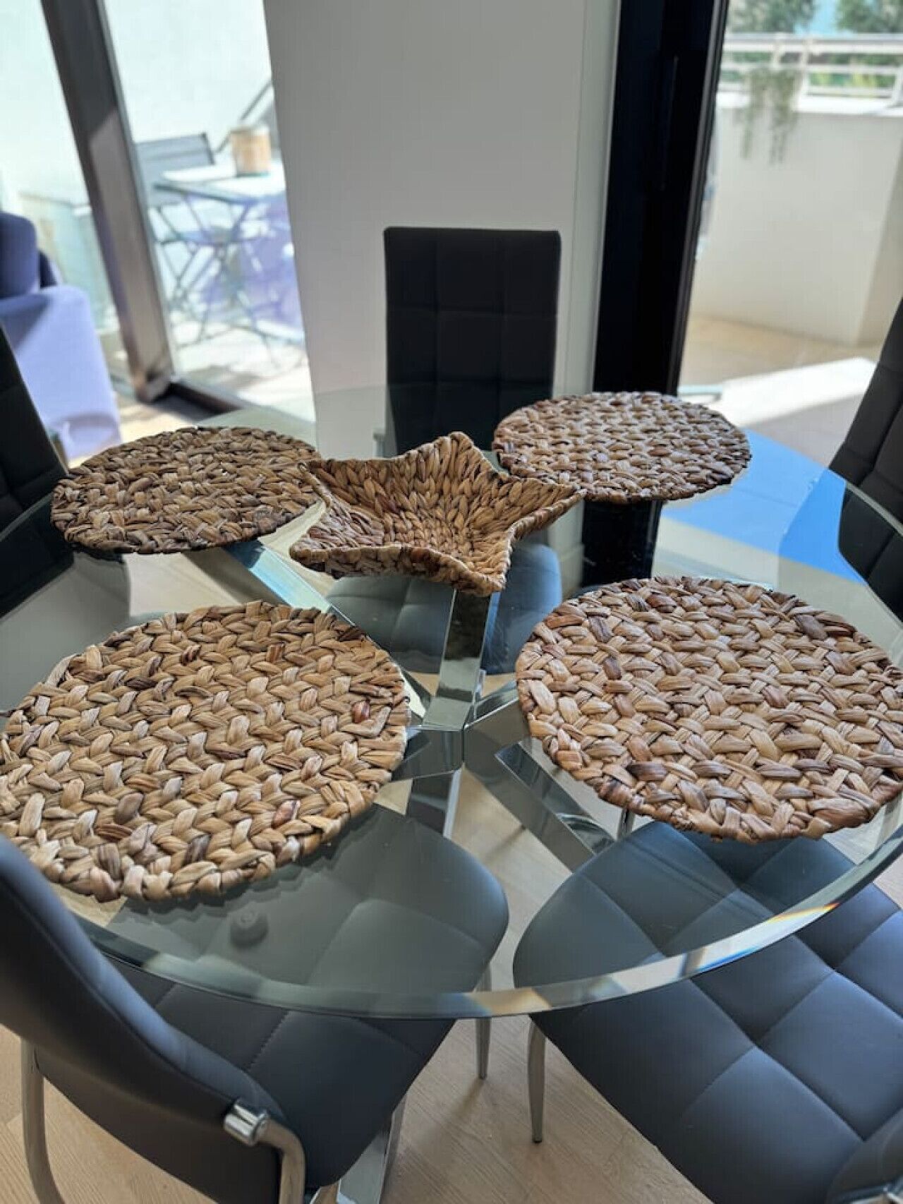 Un comedor moderno con una mesa de vidrio rodeada de sillas negras, con individuales tejidos.
