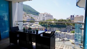 A balcony with a table and chairs, overlooking a cityscape with buildings and a hill. - Gibraltar Luxury w/ Rooftop Pools & Views (Gibraltar)