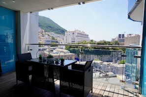 A balcony with a table and chairs, overlooking a cityscape with buildings and a hill. - Gibraltar Luxury w/ Rooftop Pools & Views (Gibraltar)