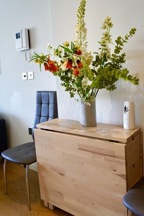 A room with a wooden desk, a chair, a vase with flowers, and a white wall with a thermostat and light switch. - Gibraltar Luxury w/ Rooftop Pools & Views (Gibraltar)