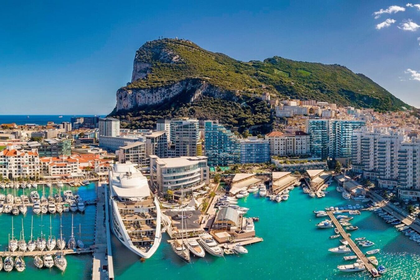 Een kuststadsbeeld met een opvallende berg, een jachthaven vol boten en moderne wolkenkrabbers.