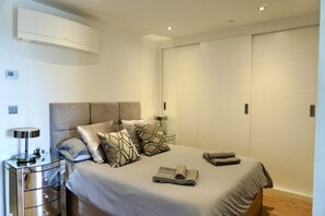 Ein modernes Schlafzimmer mit Bett, Nachttisch, Lampe und Klimaanlage.