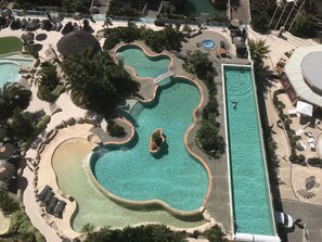 Eine Luftaufnahme eines Resorts mit mehreren Schwimmbecken, darunter ein großes rechteckiges Becken und einige kleinere, unterschiedlich gestaltete Becken.