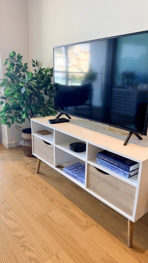 A modern living room with a flat-screen TV on a white TV stand, a potted plant, and a bookshelf with books. - Gibraltar Luxury w/ Rooftop Pools & Views (Gibraltar)