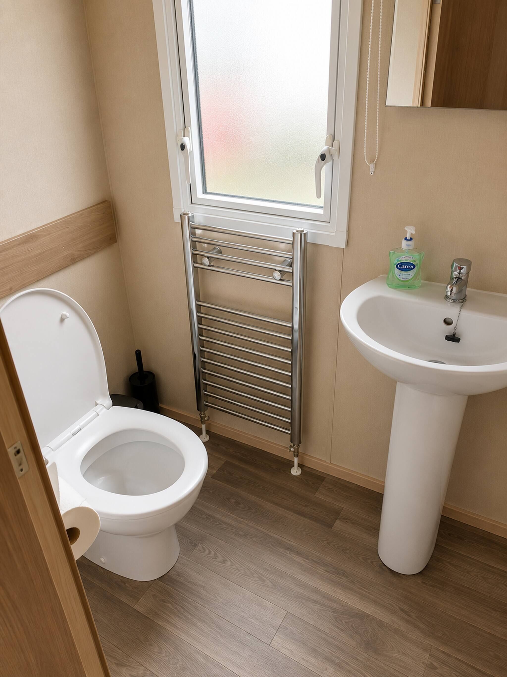 Ein Badezimmer mit Toilette, Waschbecken, einer Seifenspender und einem Fenster.