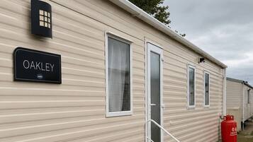 Une maison mobile avec une plaque portant le nom « OAKLEY » et une bouteille de gaz rouge à l’extérieur.