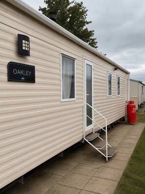 A mobile home with a nameplate reading 'OAKLEY' and a red gas cylinder outside.