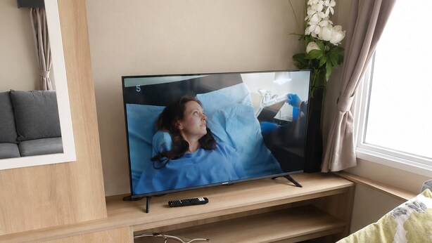 Una sala de estar con un televisor de pantalla plana sobre un soporte de madera, un sofá y una pequeña mesa con un control remoto.