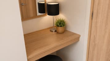 Une pièce avec un bureau en bois, une lampe noire, une petite plante en pot, un pouf noir et un miroir au mur.