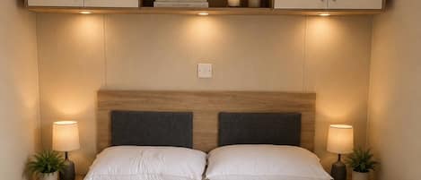 A neatly made bed with a headboard, two bedside tables with lamps, and a shelf above the bed.