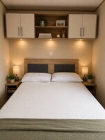 A neatly made bed with a headboard, two bedside tables with lamps, and a shelf above the bed.