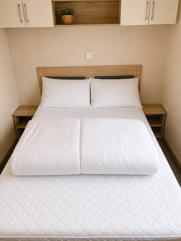 A neatly made bed with a quilted mattress, wooden headboard, and two bedside tables with lamps.