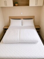 Una cama bien tendida con un colchón acolchado, cabecera de madera y dos mesitas de noche con lámparas.