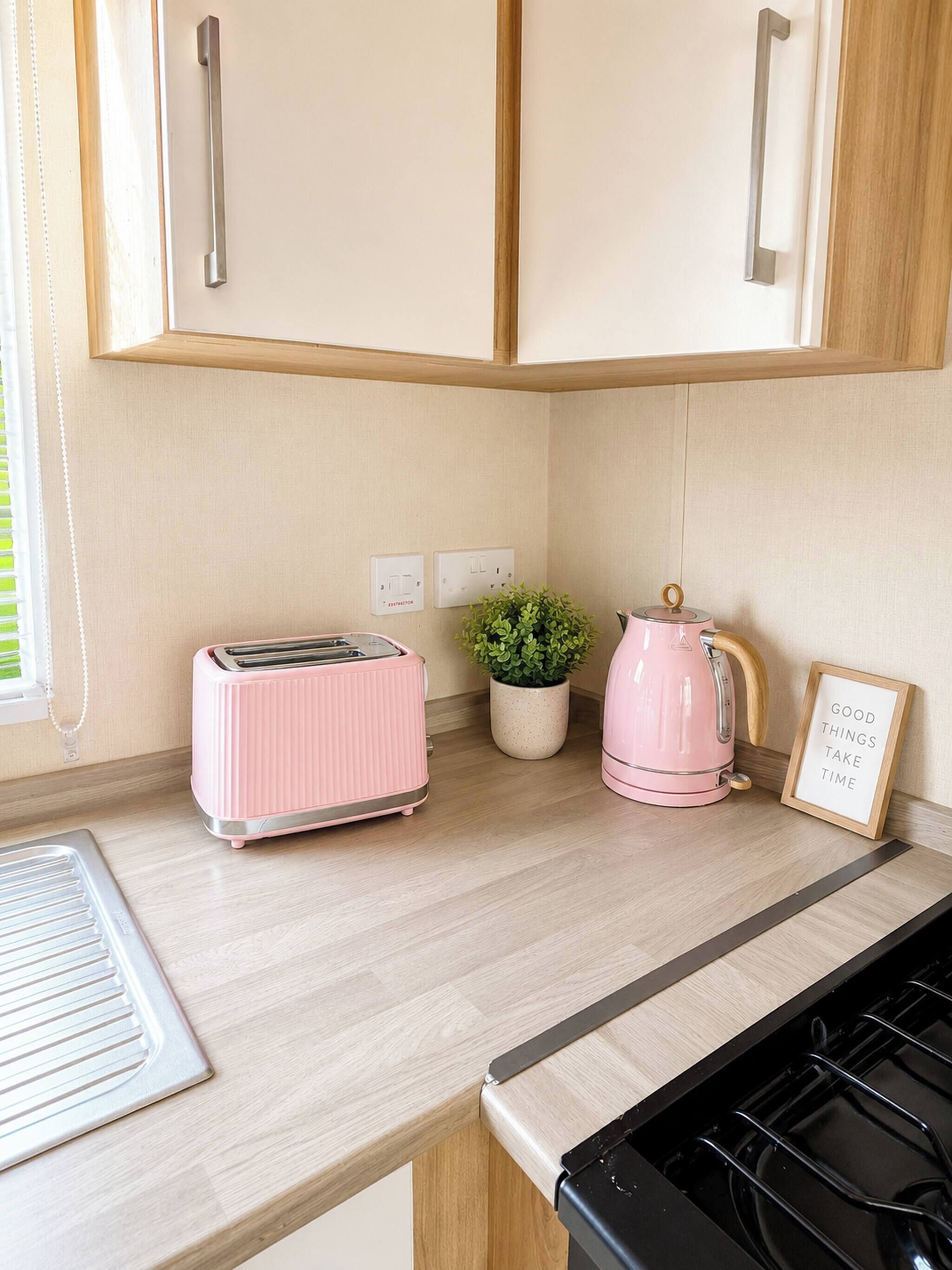 A kitchen with wooden cabinets, a pink toaster, a kettle, and a potted plant.