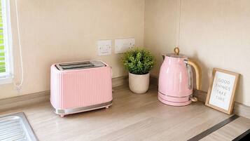 A kitchen with wooden cabinets, a pink toaster, a kettle, and a potted plant.