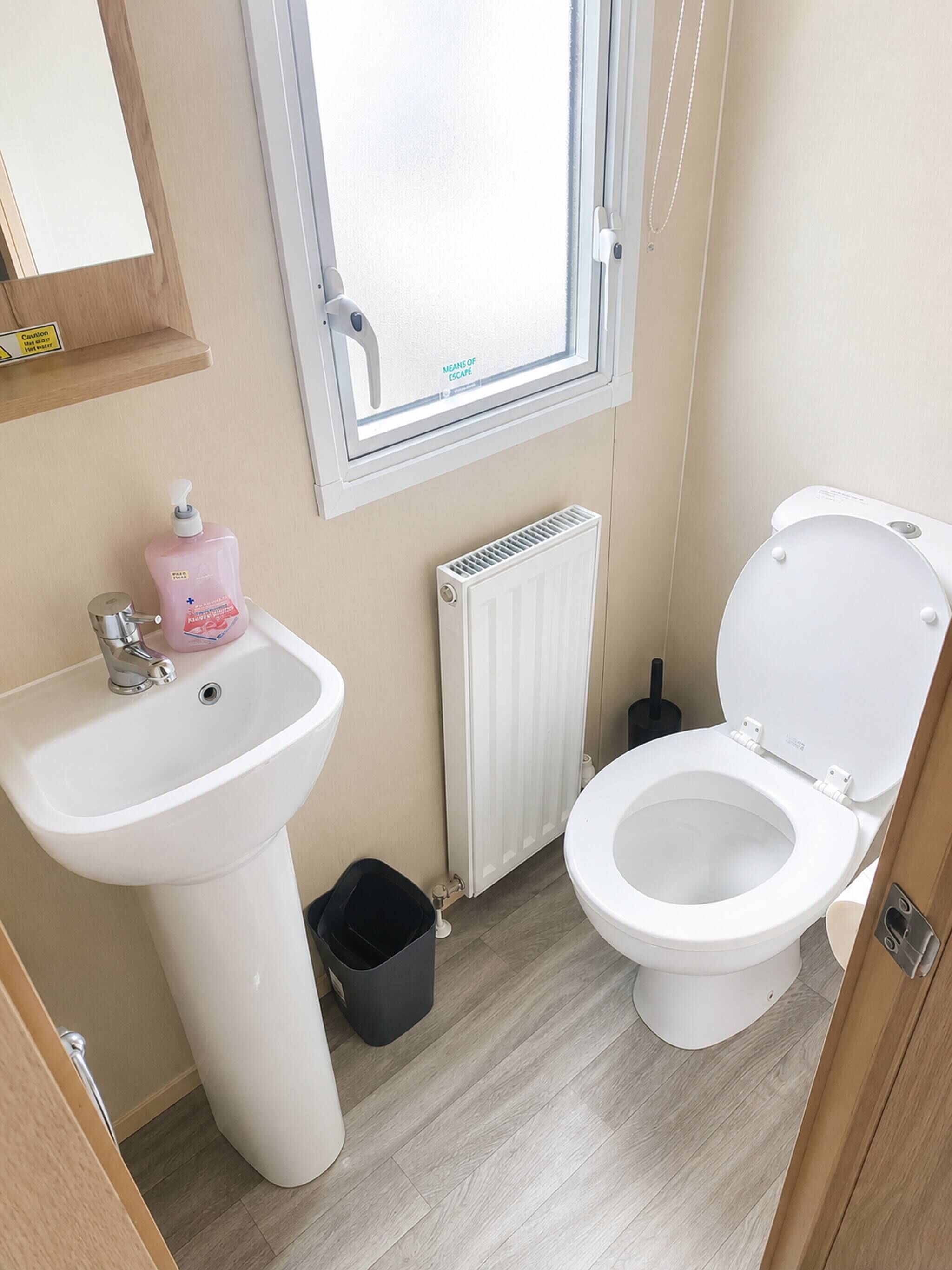 A bathroom with a white sink, a toilet, a window, and a radiator.