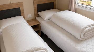 Une chambre avec deux lits, une tête de lit en bois, une table de chevet et une fenêtre avec des rideaux.