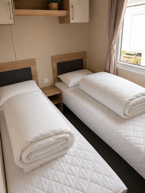 A bedroom with two beds, a wooden headboard, a nightstand, and a window with curtains.