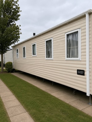 A row of mobile homes with a grassy lawn and a paved walkway.