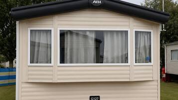 A mobile home with a flat roof, three windows with curtains, and a visible identification number G127.