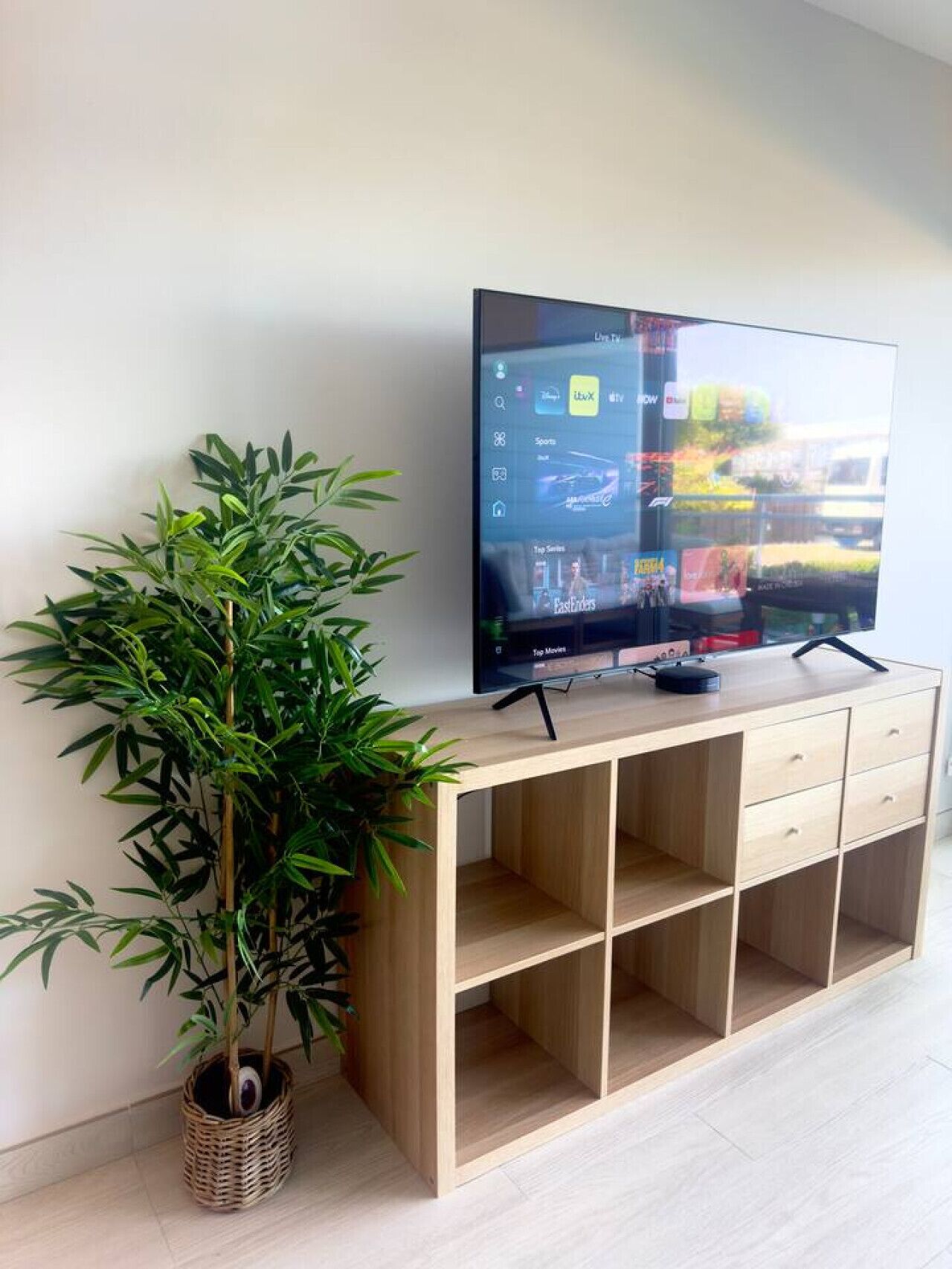 Een televisie op een houten standaard, met een bamboe plant ernaast.