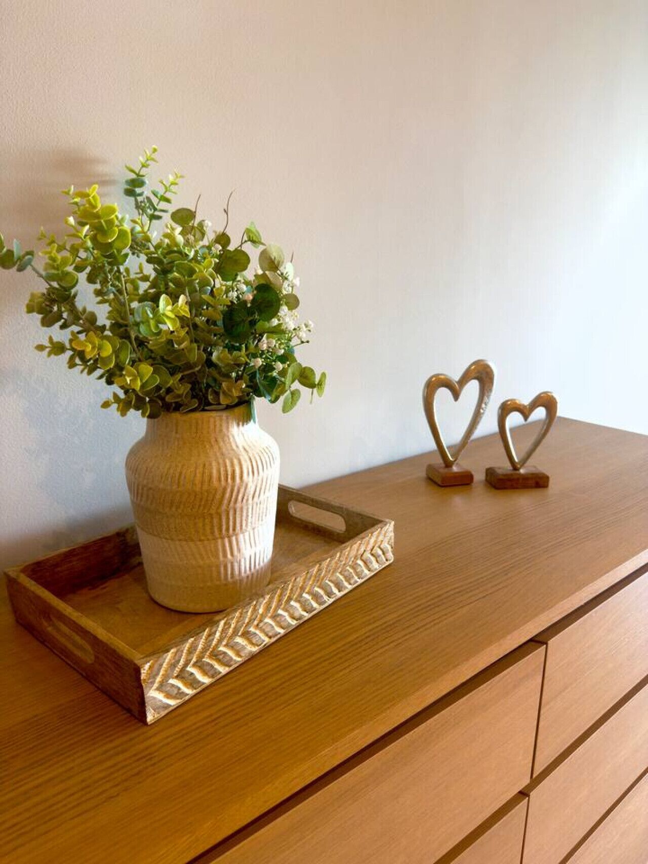 A wooden dresser with a vase of green foliage and two heart-shaped decorations on top.
