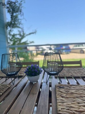 Ein Holztisch mit zwei Drahtkerzenhaltern und einem Blumentopf mit violetten Blüten.