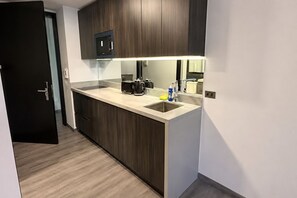 A modern kitchen with dark wood cabinets, a stainless steel sink, and a built-in microwave. - Studio with King-Size Bed, Gym, Coworking Space, and Fast Check-In (Santiago)