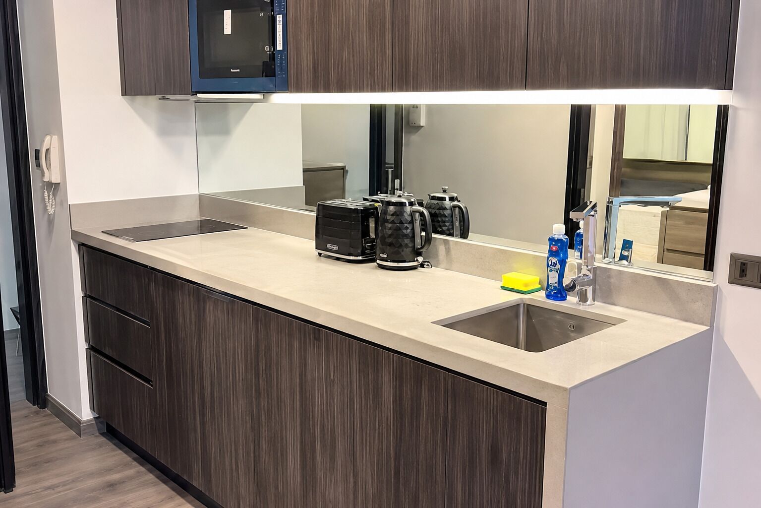Una cocina moderna con un lavamanos doble, gabinetes de madera oscura, un microondas y una cafetera.