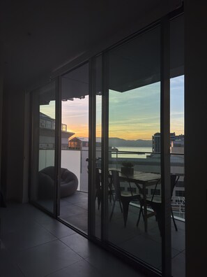Ein modernes Interieur mit einer Schiebeglasdoor zu einem Balkon mit Tisch und Stühlen, mit Blick auf ein Gewässer und entfernte Gebäude.