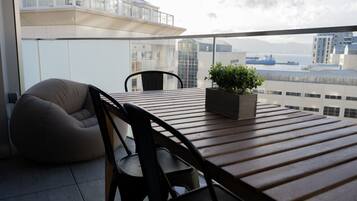 A balcony with a wooden table, two chairs, a bean bag, and a potted plant.