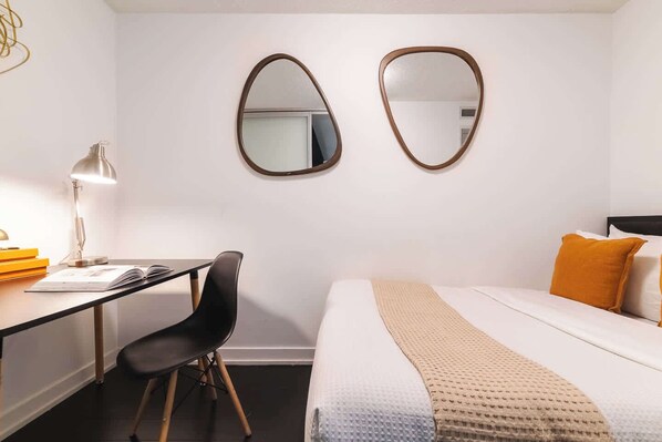 A hotel room with a desk, chair, bed, and two wall-mounted mirrors.