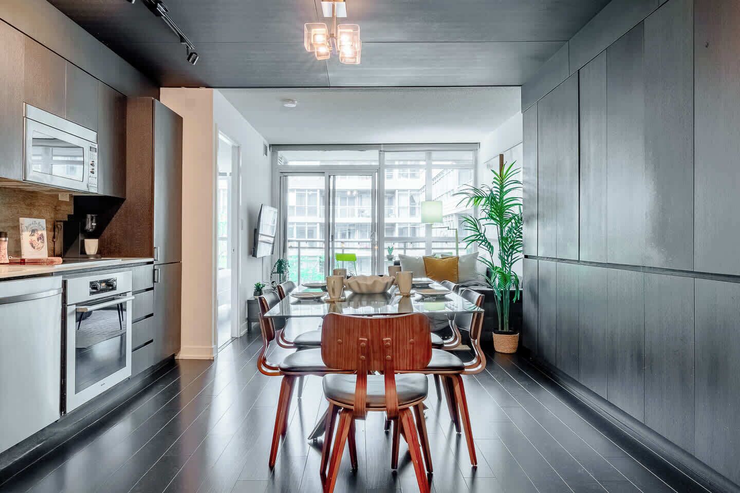 A modern kitchen with a dining area, featuring a large window, stainless steel appliances, and a wooden dining table.