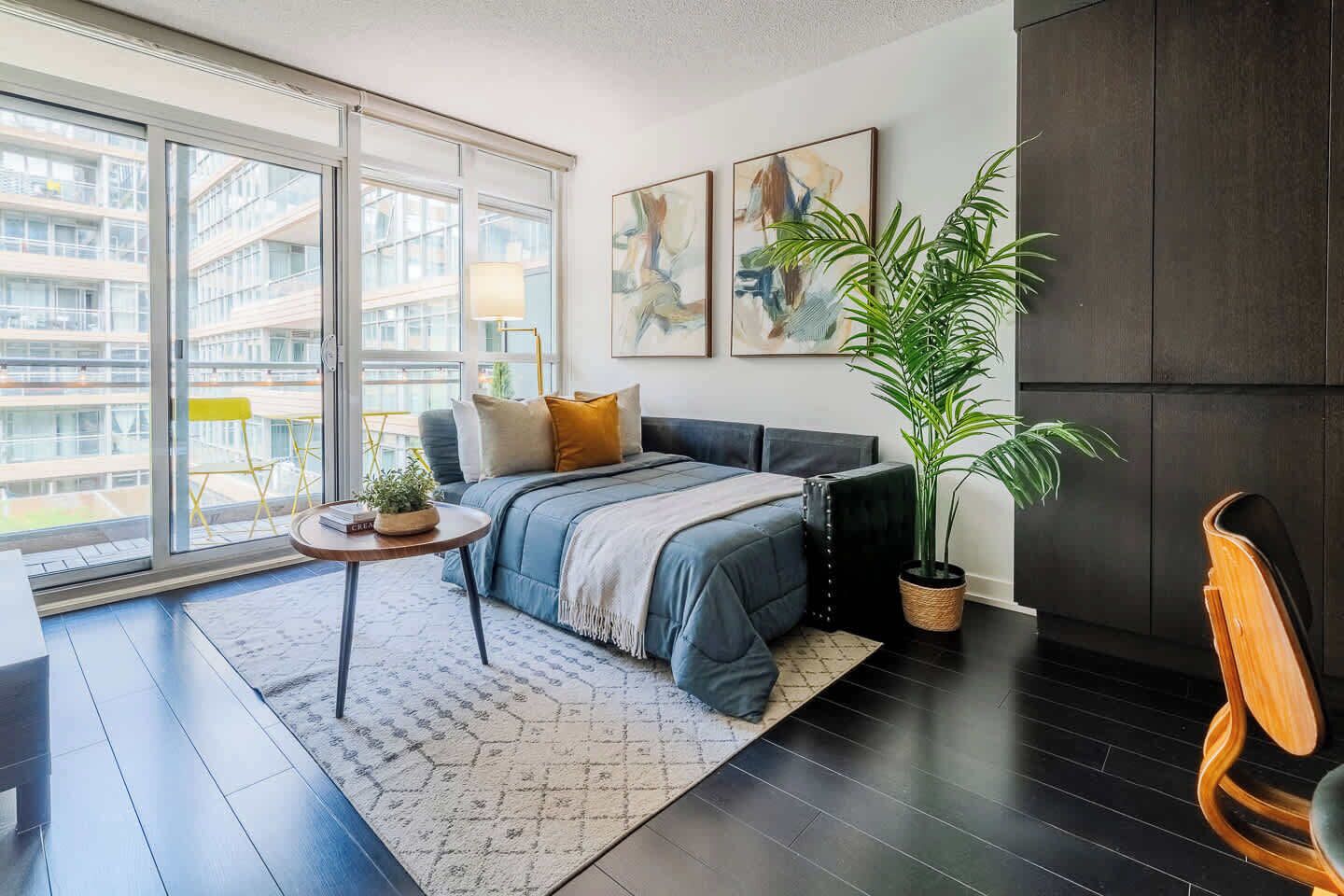 A modern bedroom with a large window, a bed, a small table, and a potted plant.