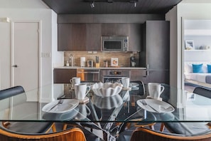 A modern kitchen with dark wood cabinets, stainless steel appliances, and a glass dining table set for six.