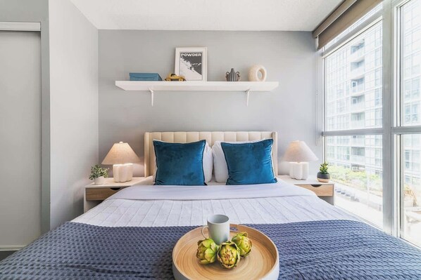 A modern bedroom with a bed, bedside lamps, a window with a view, and a shelf with decorative items.