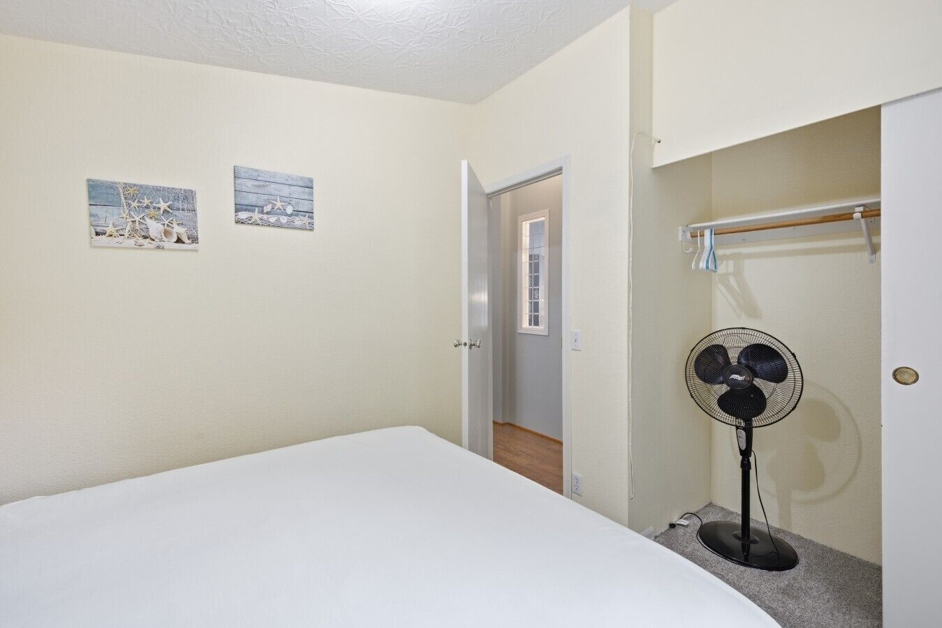A bedroom with a bed, a standing fan, and two wall art pieces.