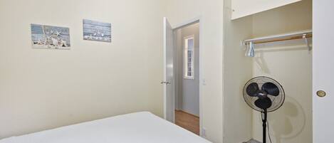 A bedroom with a bed, a standing fan, and two wall art pieces.